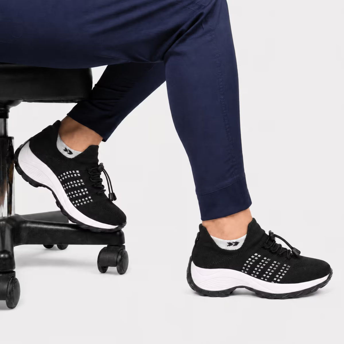 Black lace-up comfort sneaker with white dot pattern, worn with navy pants